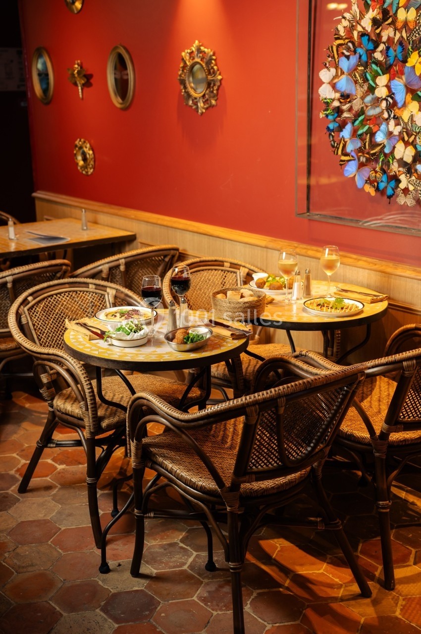 Tables en rotin dressées avec des assiettes et des verres de vin dans un restaurant à la décoration murale colorée.