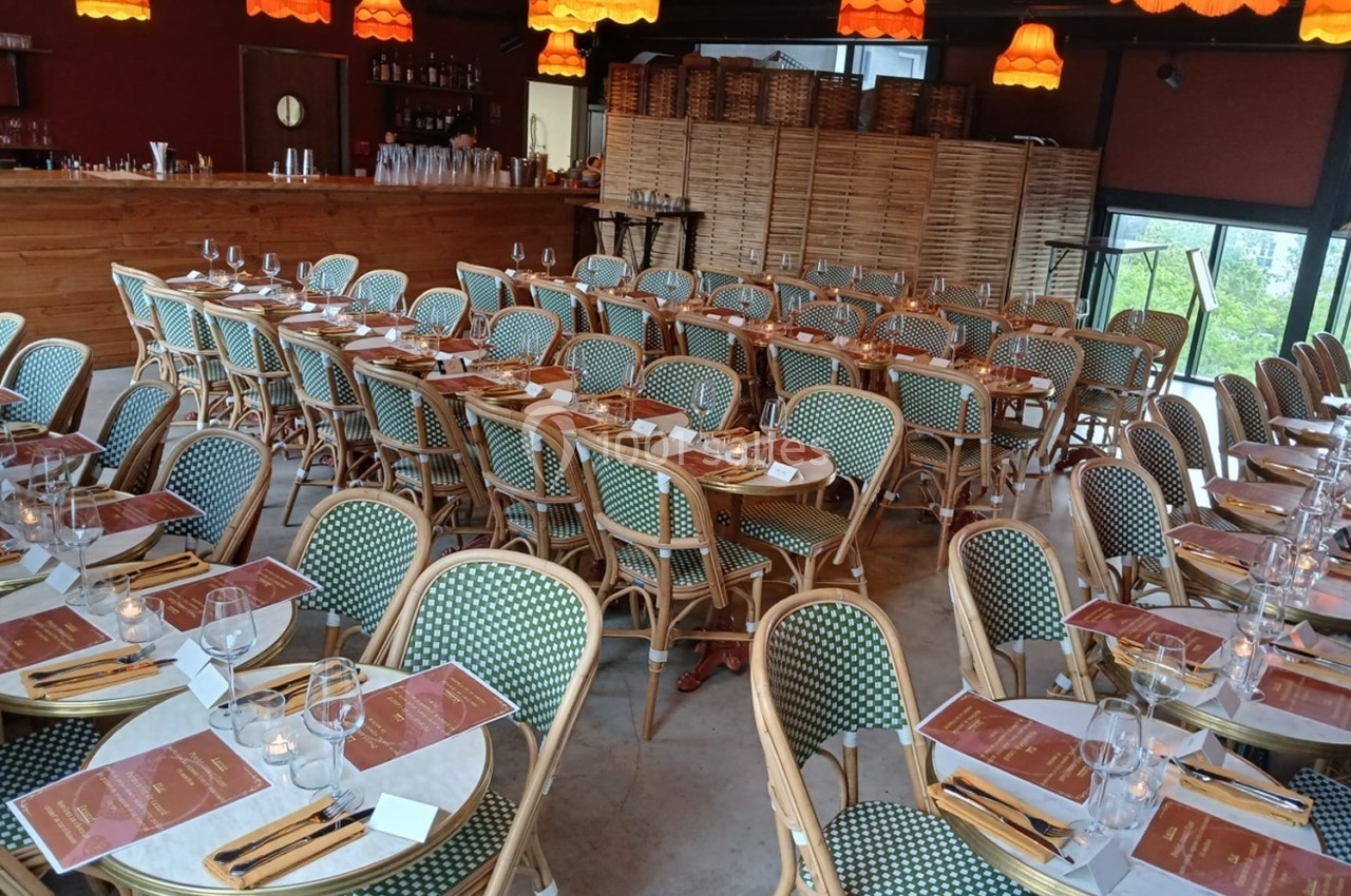 Salle de restaurant avec tables dressées, chaises en osier et lampes suspendues orange dans une ambiance chaleureuse.