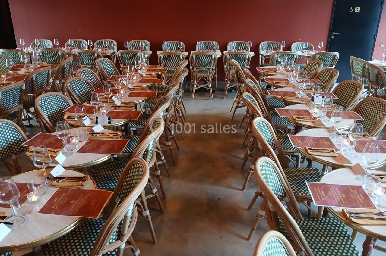Salle de restaurant avec des tables dressées, alignées, couvertes de nappes blanches, menus et verres à vin.