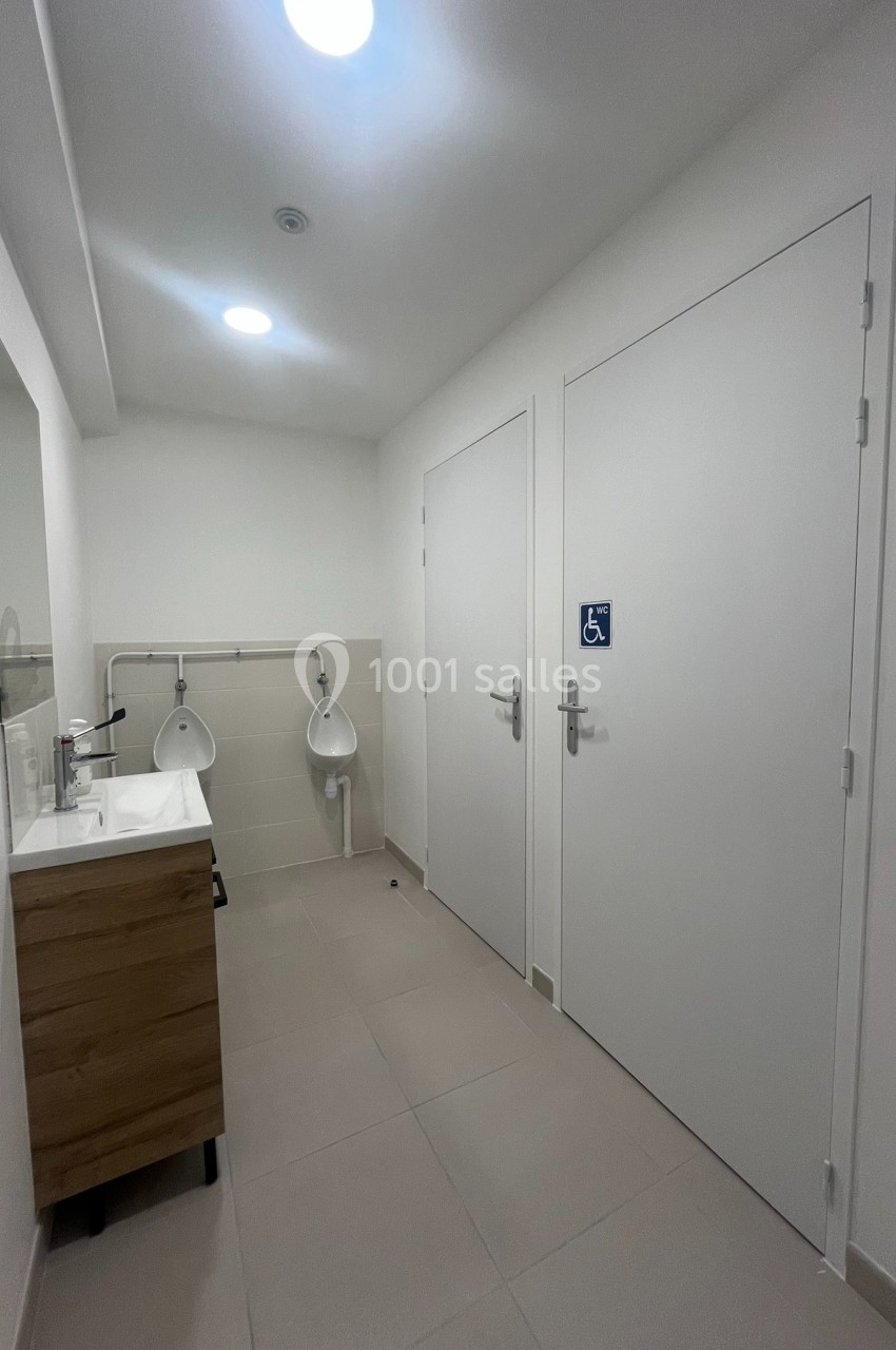 Toilettes accessibles avec lavabo, urinoirs et porte signalée pour personnes à mobilité réduite.