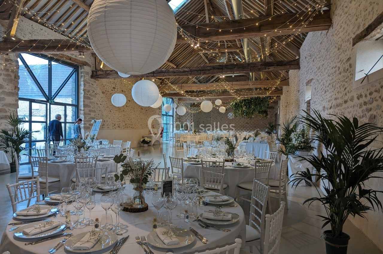 Salle de réception décorée avec des tables rondes dressées, des lanternes suspendues et des plantes vertes.