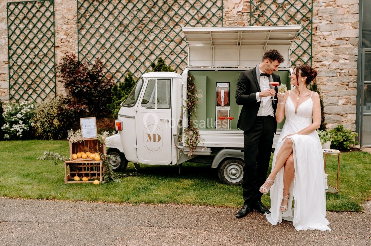 Un couple élégant trinque devant un petit camion-bar décoré, stationné dans un jardin.