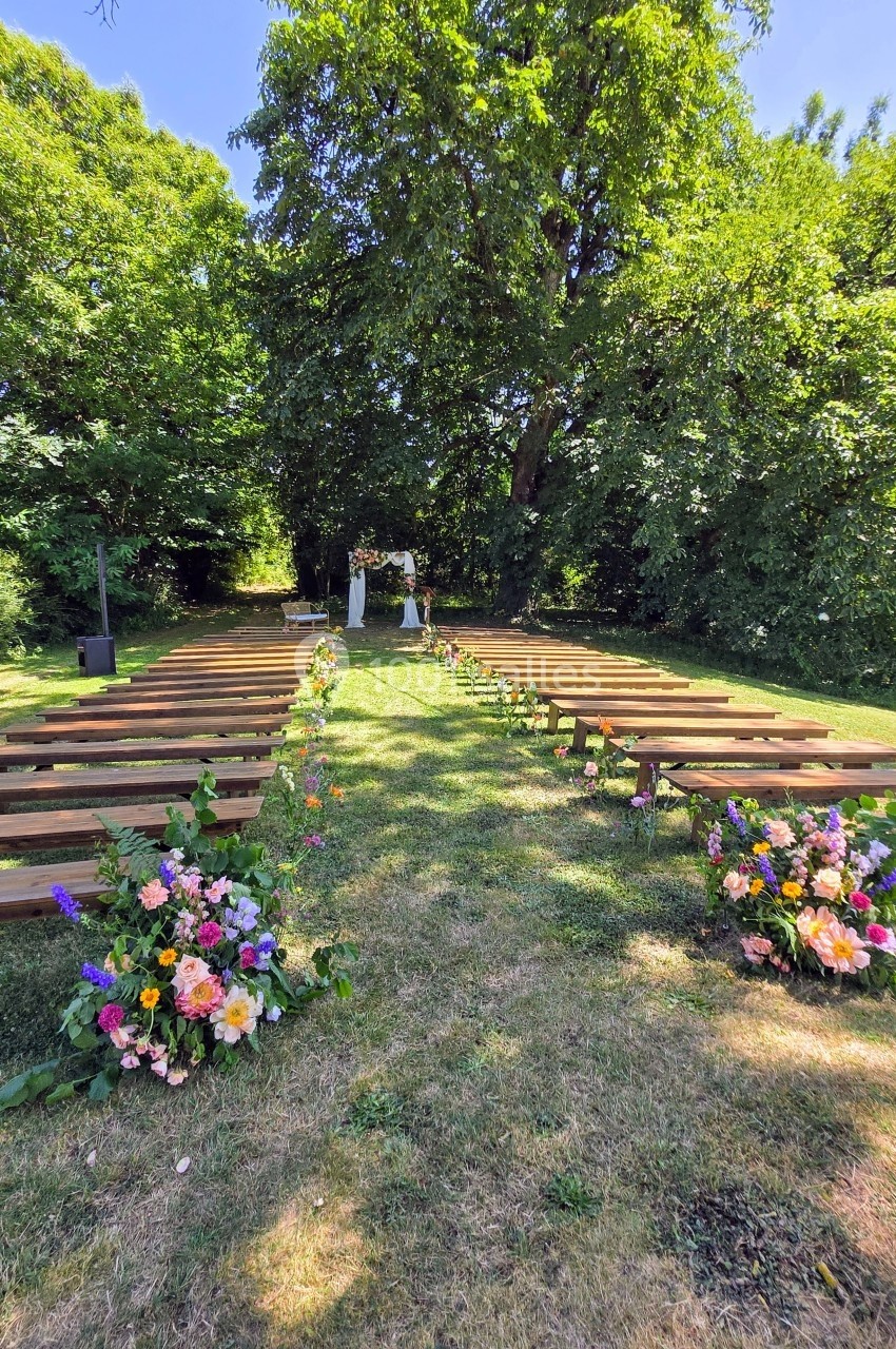 Allée centrale bordée de bancs en bois et de fleurs colorées, menant à un autel dans un jardin verdoyant.