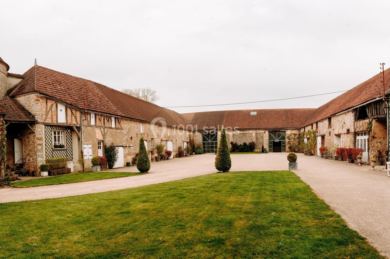 Cour intérieure d'un bâtiment ancien en pierre avec toits en tuiles, pelouse et allée gravillonnée.