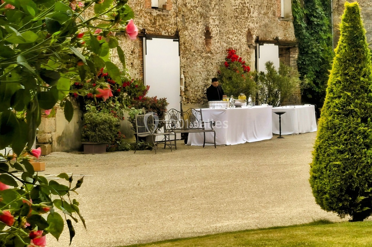 Table de buffet dressée en extérieur devant un bâtiment en pierre, entourée de végétation et de fleurs.