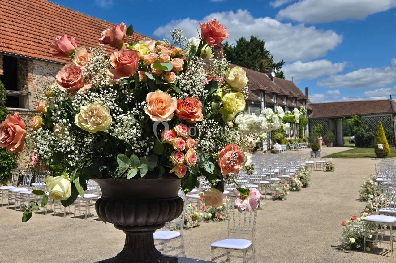 Arrangement floral avec roses et gypsophiles dans une cour extérieure aménagée pour une cérémonie, sous un ciel bleu.