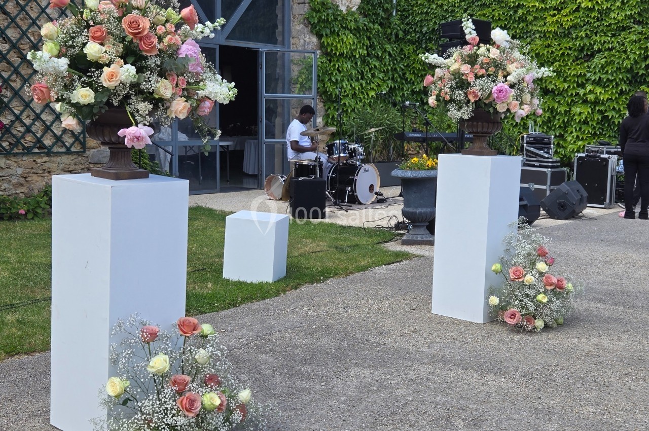 Arrangements floraux colorés sur des socles blancs en extérieur, avec un batteur et des équipements en arrière-plan.