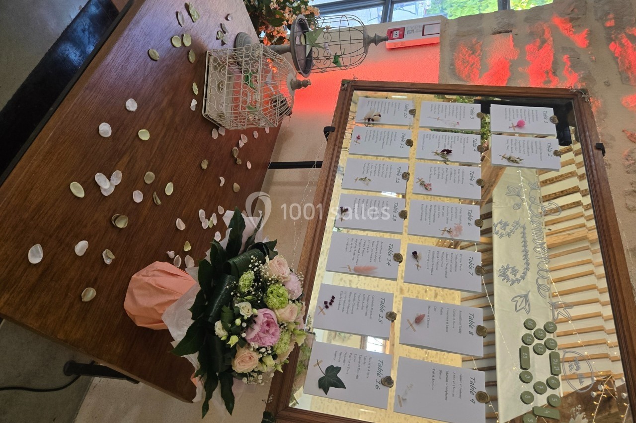 Tableau de plan de table de mariage avec cartes nominatives, décor floral et pétales dispersés sur une table en bois.