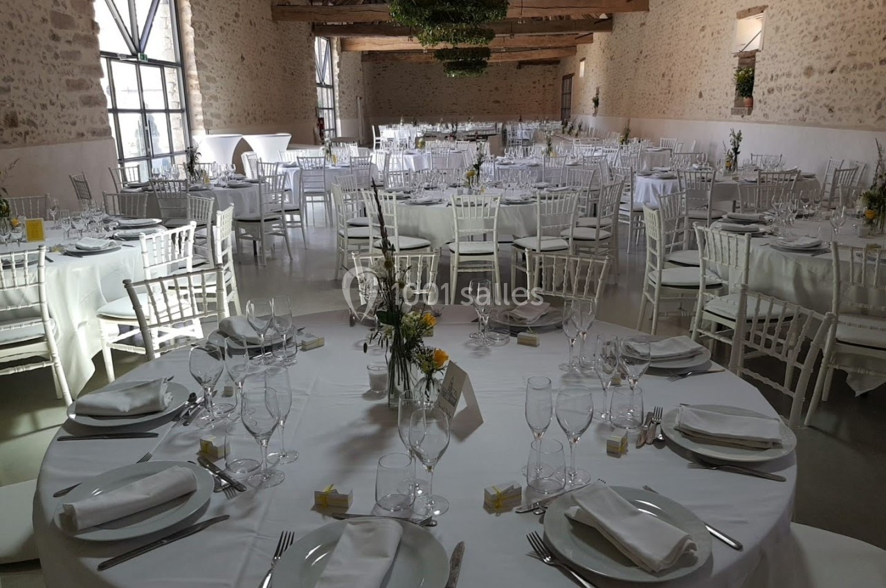 Salle de réception lumineuse avec tables rondes dressées, nappes blanches et chaises en bois clair.