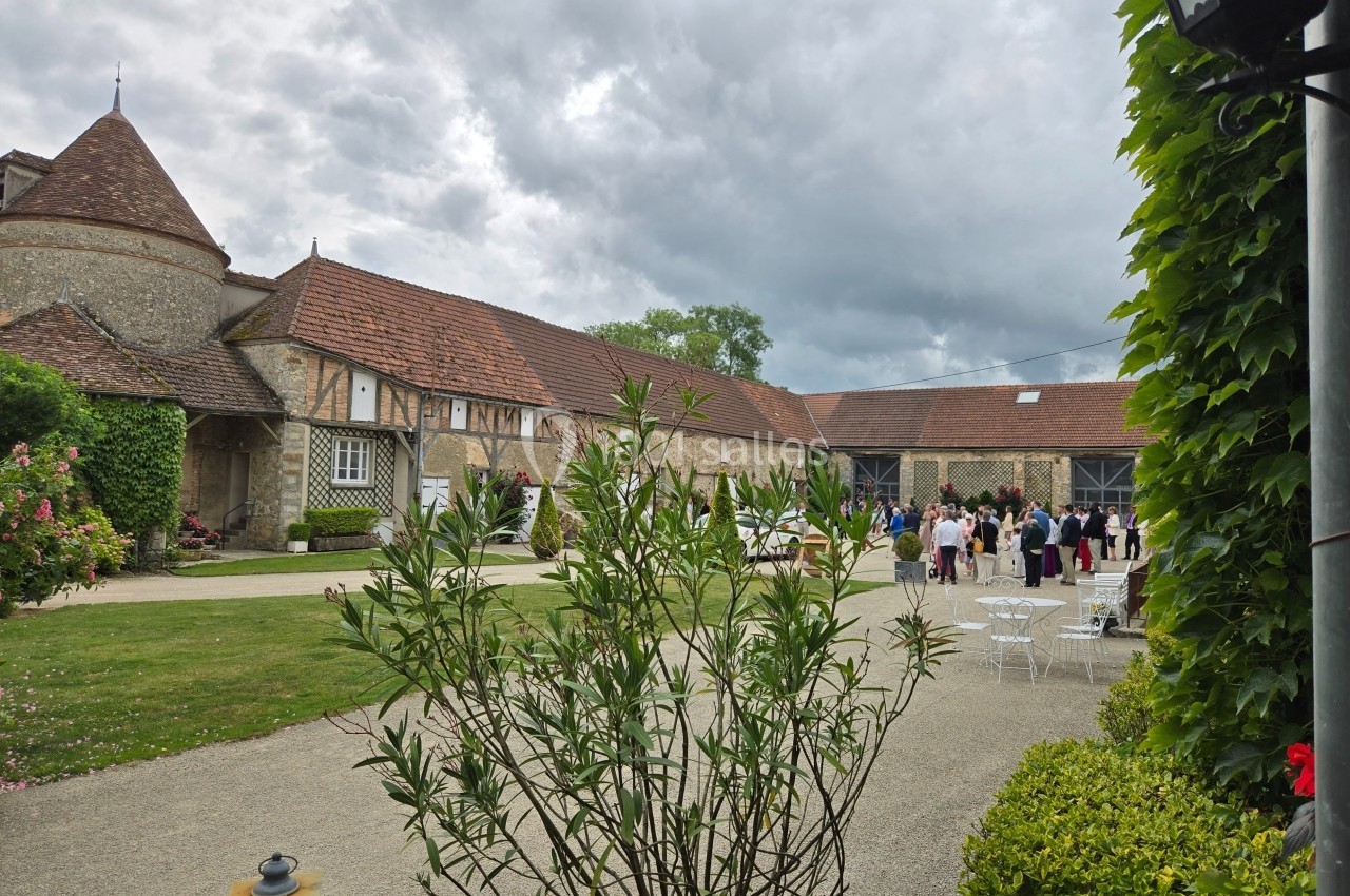 Un groupe de personnes rassemblé dans la cour d'un bâtiment en pierre avec un ciel nuageux en arrière-plan.