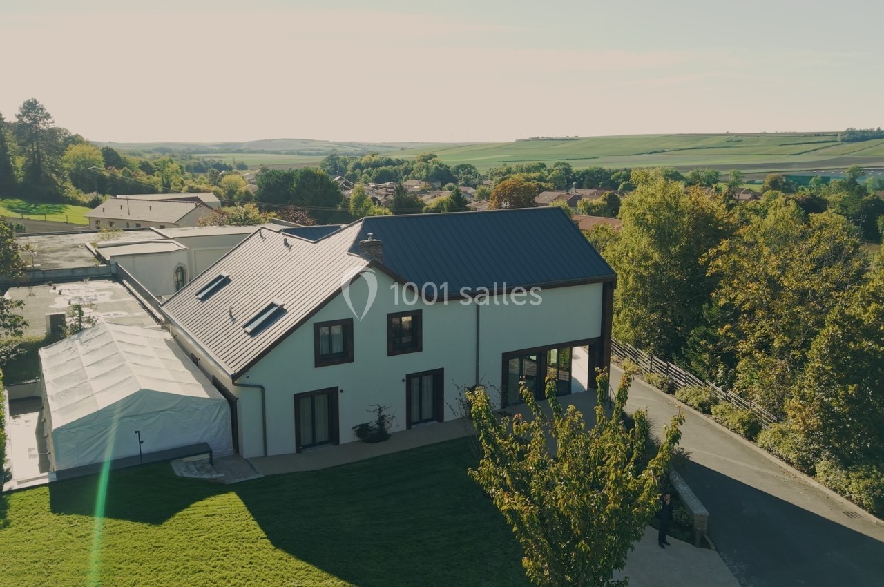 Vue aérienne d'une maison moderne avec toit en métal, entourée de verdure et d'un paysage rural.