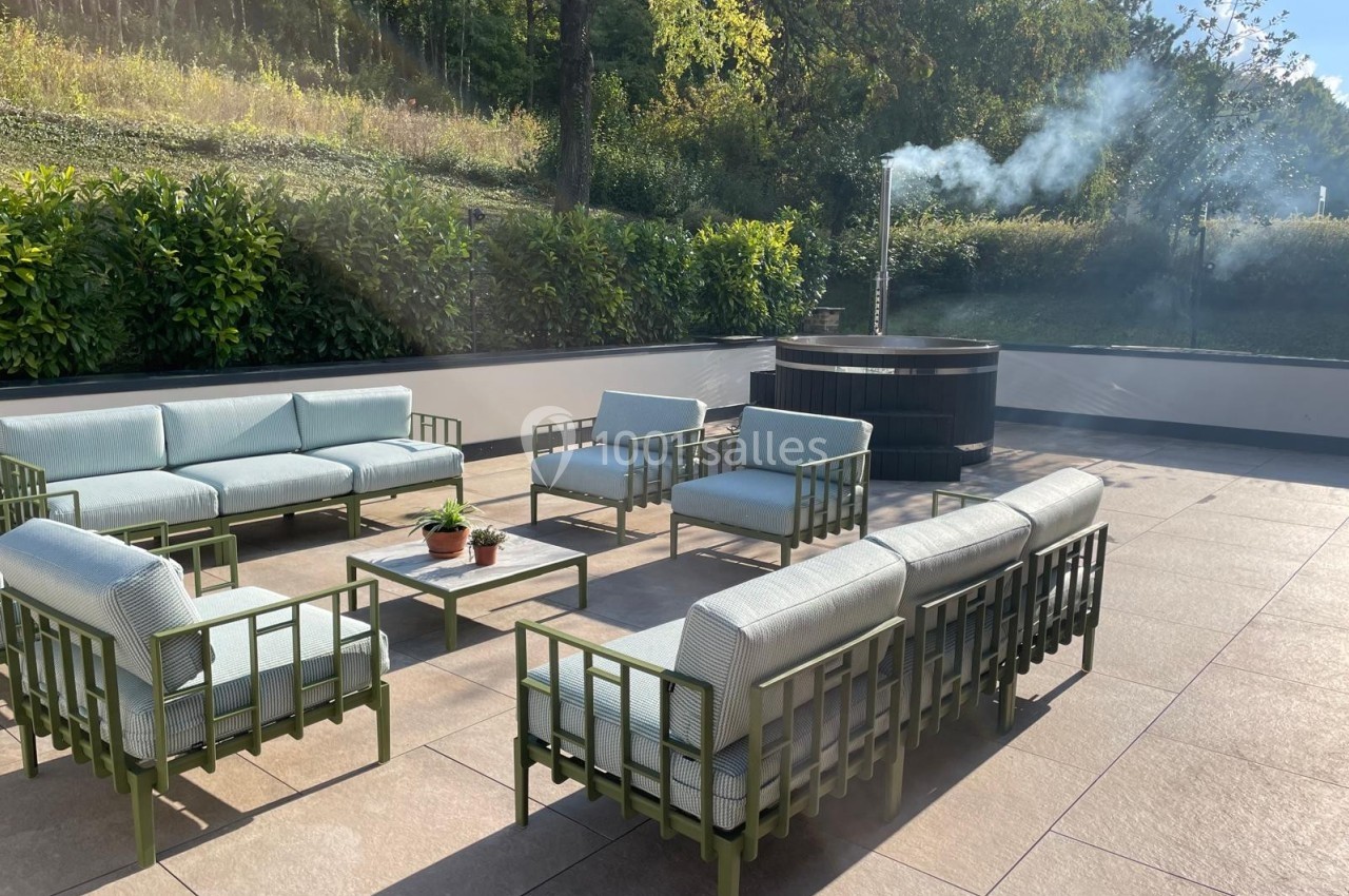 Mobilier de jardin avec canapés et fauteuils disposés autour d'une table basse, près d'un bain nordique fumant.