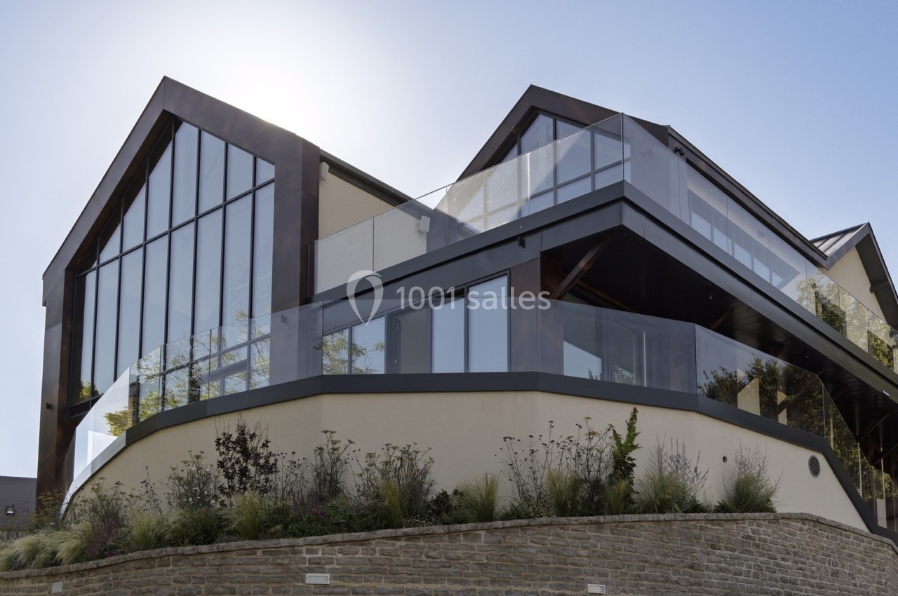 Façade moderne d'une maison avec grandes baies vitrées, balcons en verre et jardin paysager au premier plan.