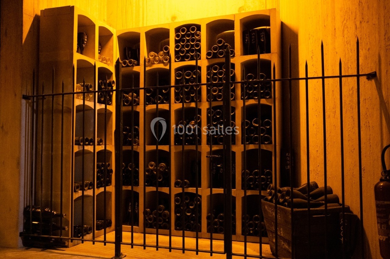 Casiers en bois remplis de bouteilles de vin, éclairés par une lumière chaude, derrière une grille métallique.