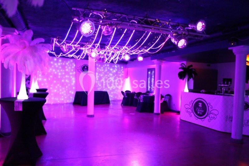 Salle de réception décorée avec des lumières violettes, des colonnes lumineuses et des tables hautes noires.