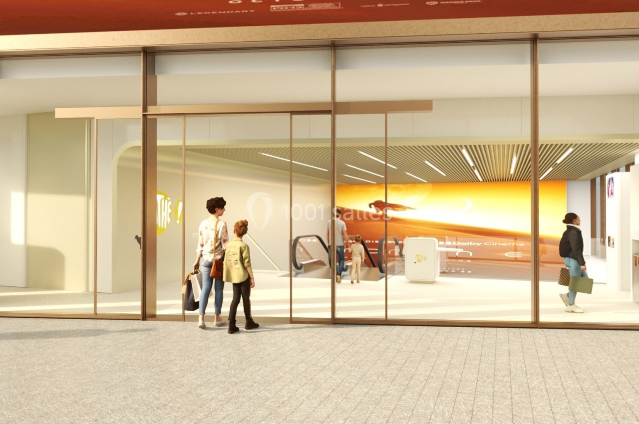 Entrée d'un espace moderne avec des portes vitrées, un écran lumineux et des personnes entrant ou sortant.