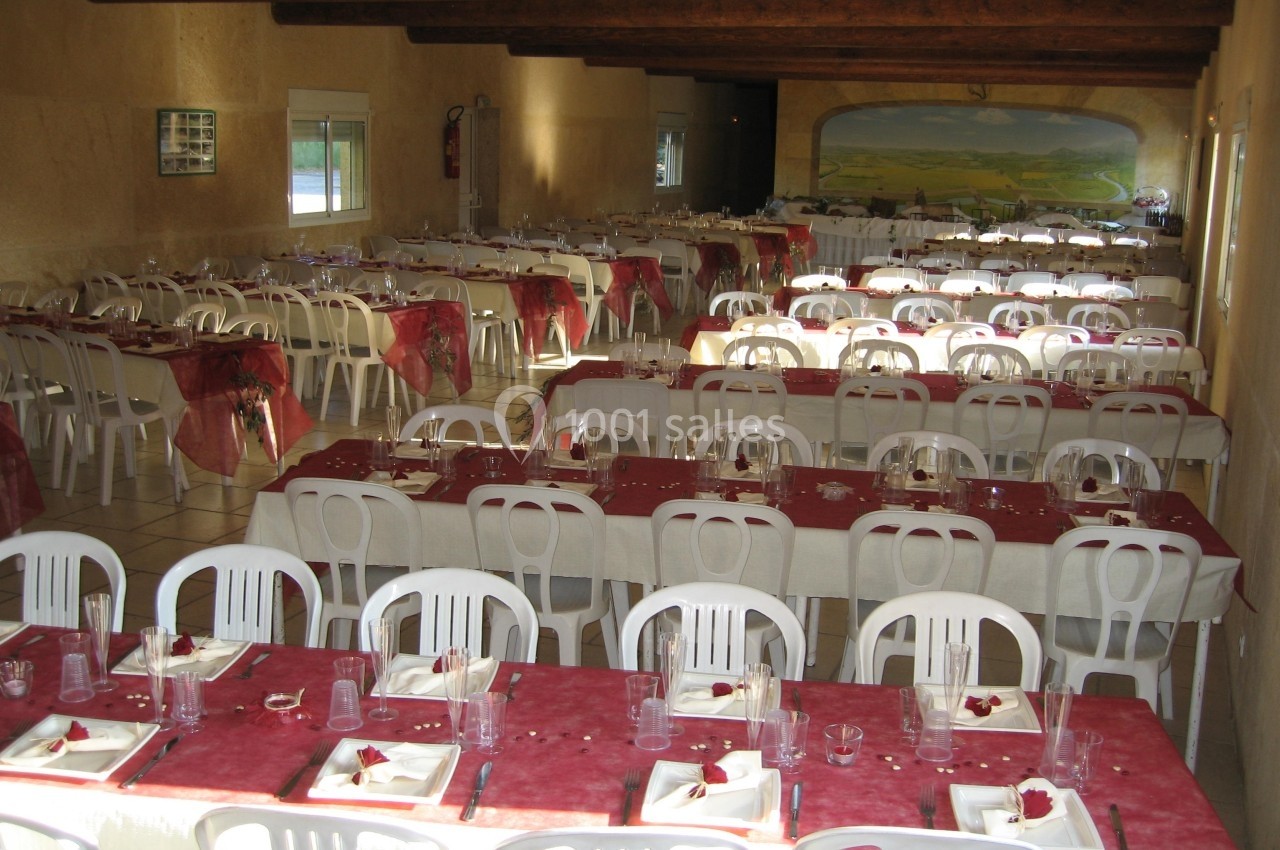 Salle de réception avec de longues tables dressées, nappes rouges et blanches, et chaises en plastique blanc.