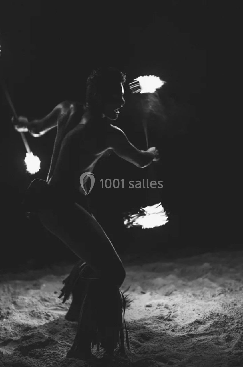 Un artiste jongle avec des torches enflammées dans l'obscurité, sur un sol sablonneux.