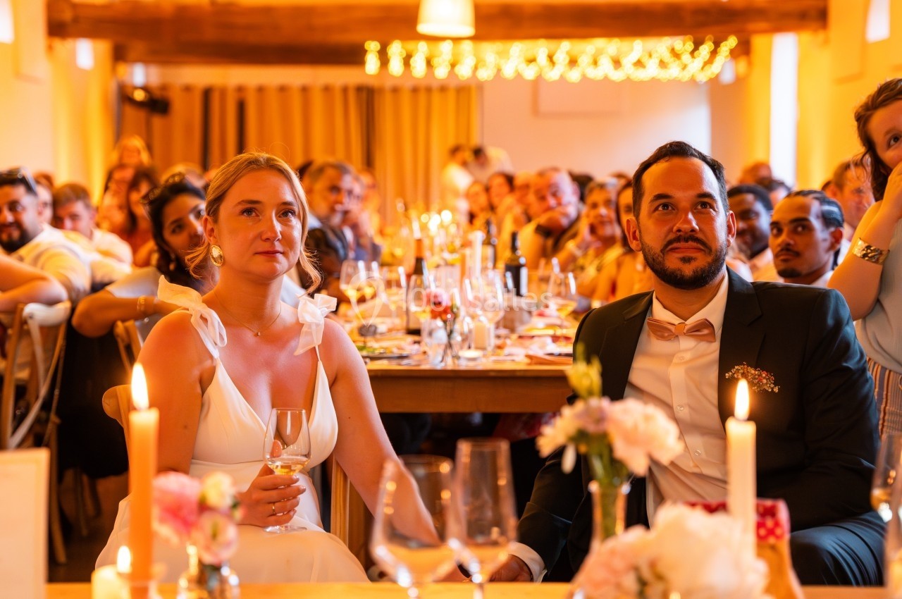 Un couple assis à une table lors d'une réception, entouré d'invités et de décorations lumineuses.