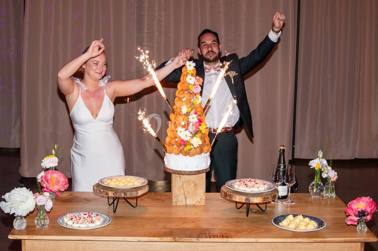 Un couple célèbre son mariage devant une pièce montée décorée de fleurs et de cierges magiques.