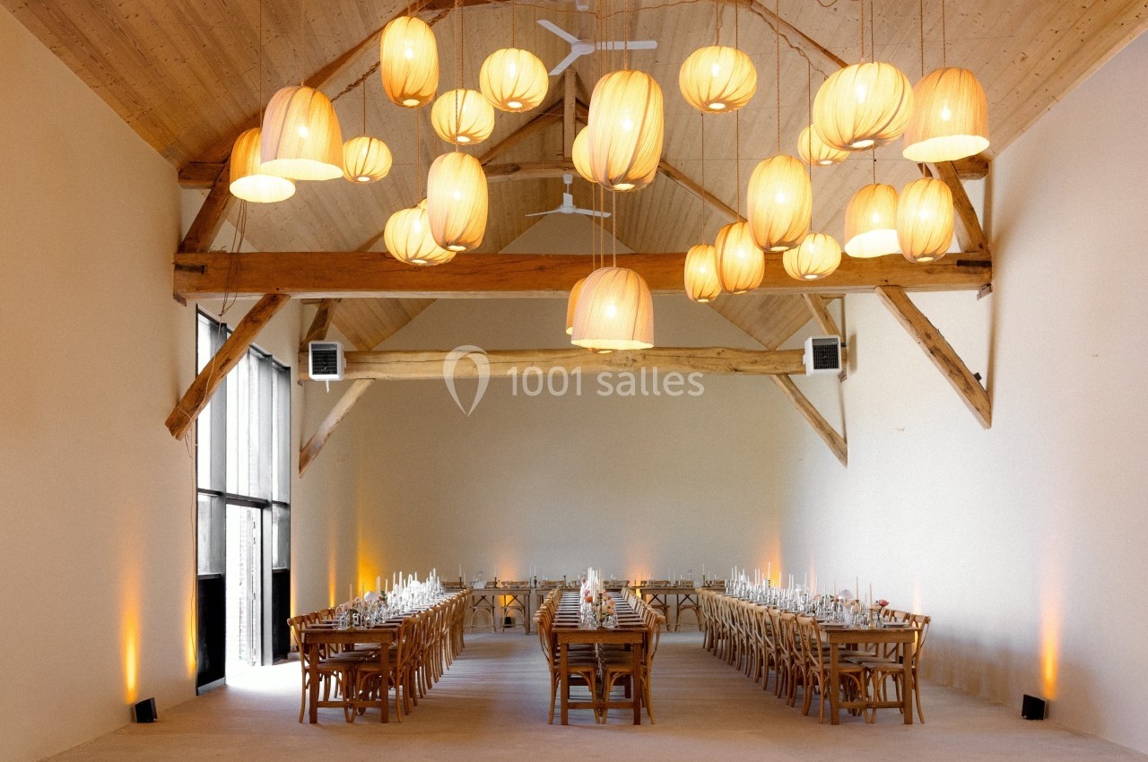 Salle lumineuse avec poutres apparentes, tables en bois alignées et suspensions en forme de lanternes.