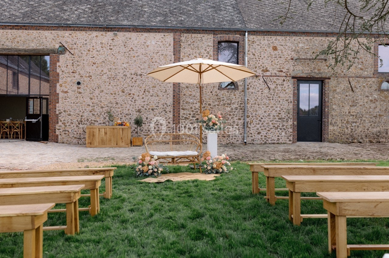 Bancs en bois disposés sur une pelouse face à un espace décoré avec un canapé, des fleurs et un parasol devant une bâtisse…