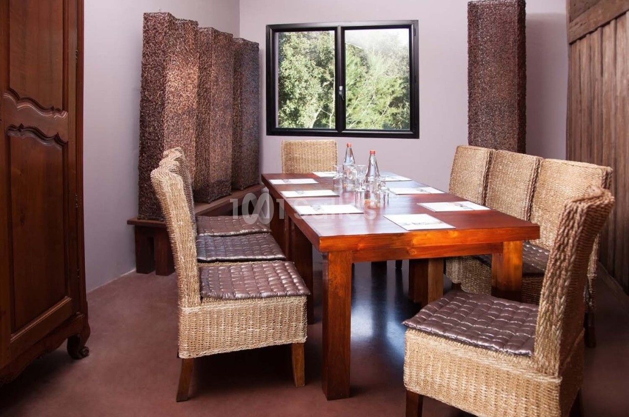 Salle de réunion avec table en bois, chaises en osier, bouteilles d'eau et fenêtre donnant sur un paysage verdoyant.