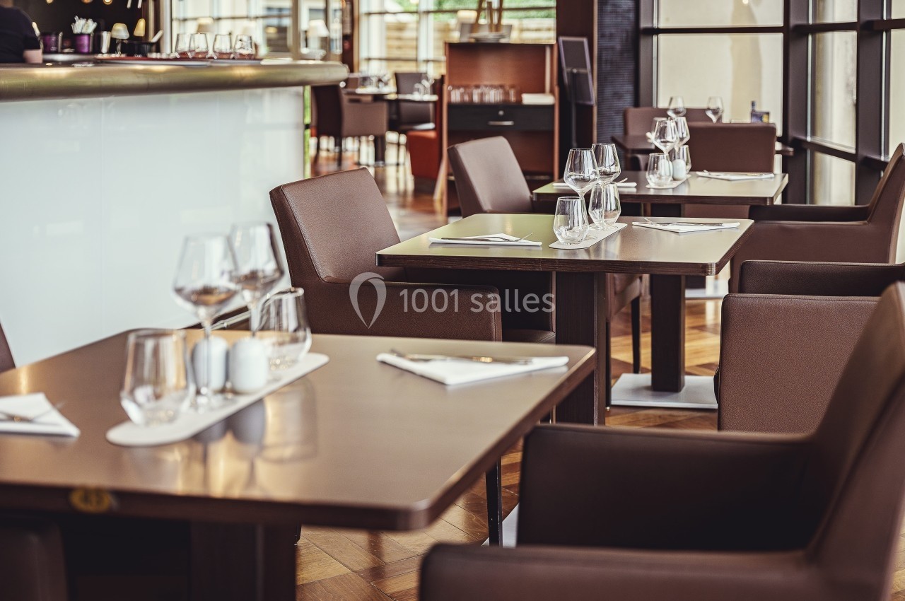 Tables de restaurant élégamment dressées avec verres et serviettes, dans un intérieur moderne et lumineux.