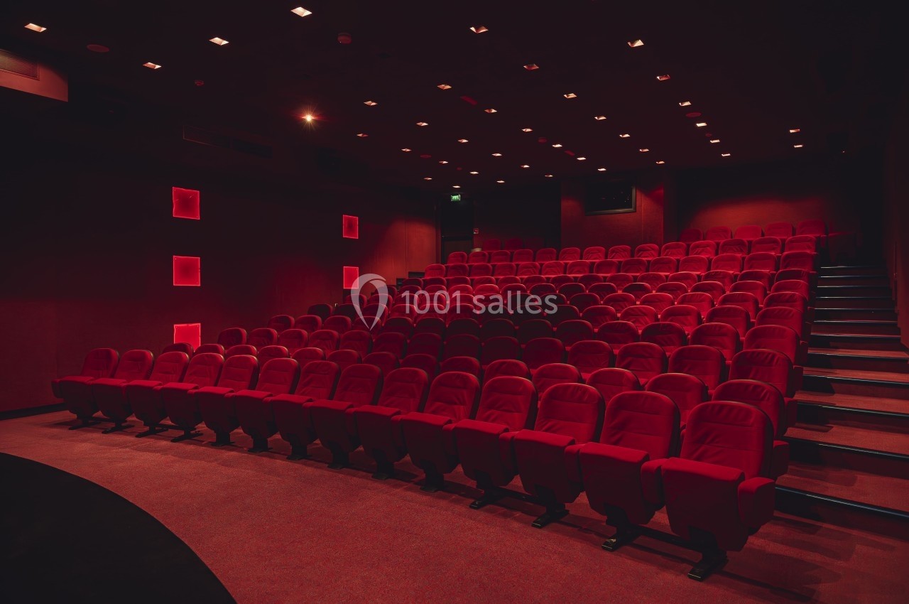Salle de cinéma vide avec rangées de fauteuils rouges et éclairage tamisé.