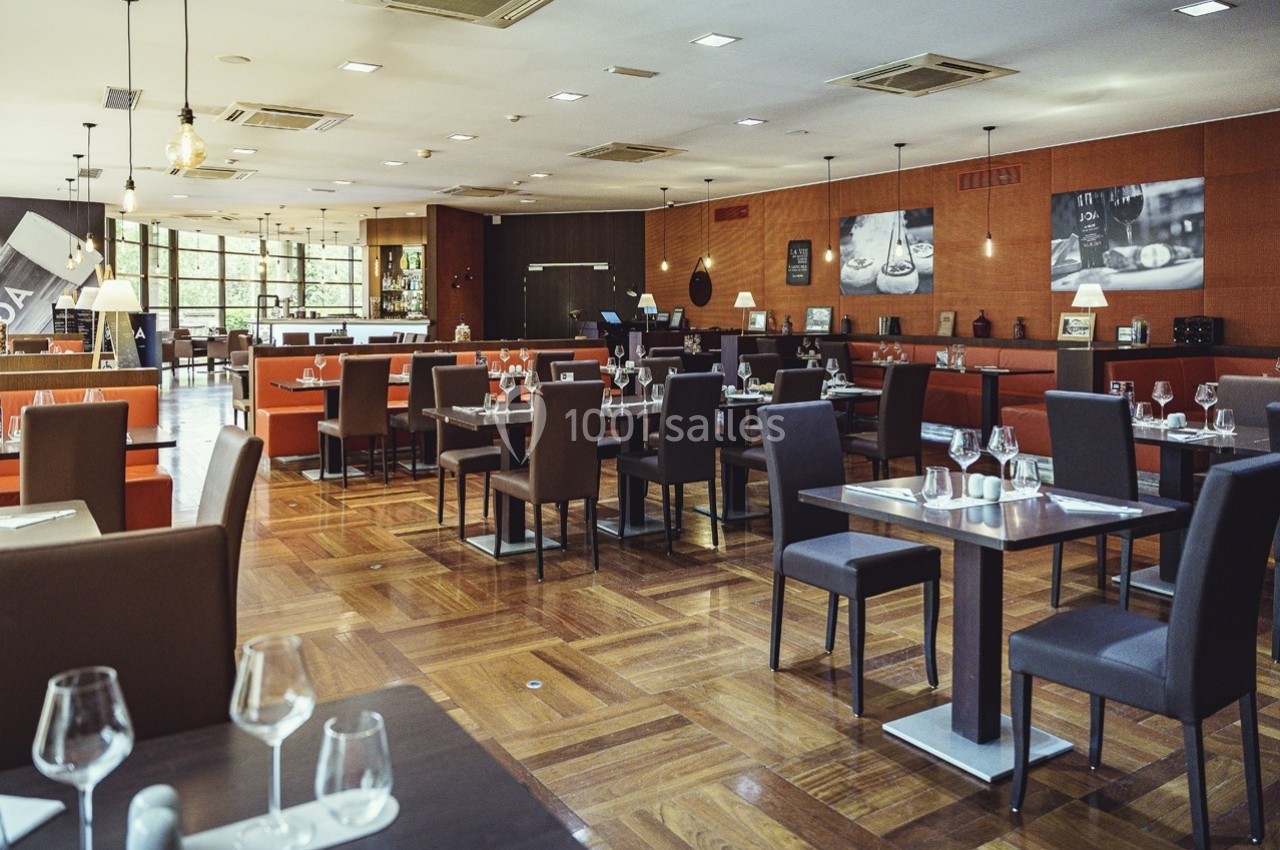 Salle de restaurant moderne avec tables dressées, chaises sombres et éclairage chaleureux.