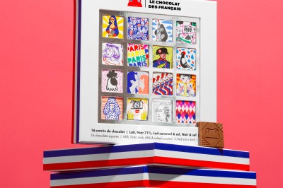 Chocolats colorés formant les mots ’Bonne Fête’ dans une boîte, une main prenant un carré décoré.