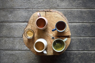 Quatre boissons chaudes variées servies dans des tasses colorées, disposées sur une table en bois rond.