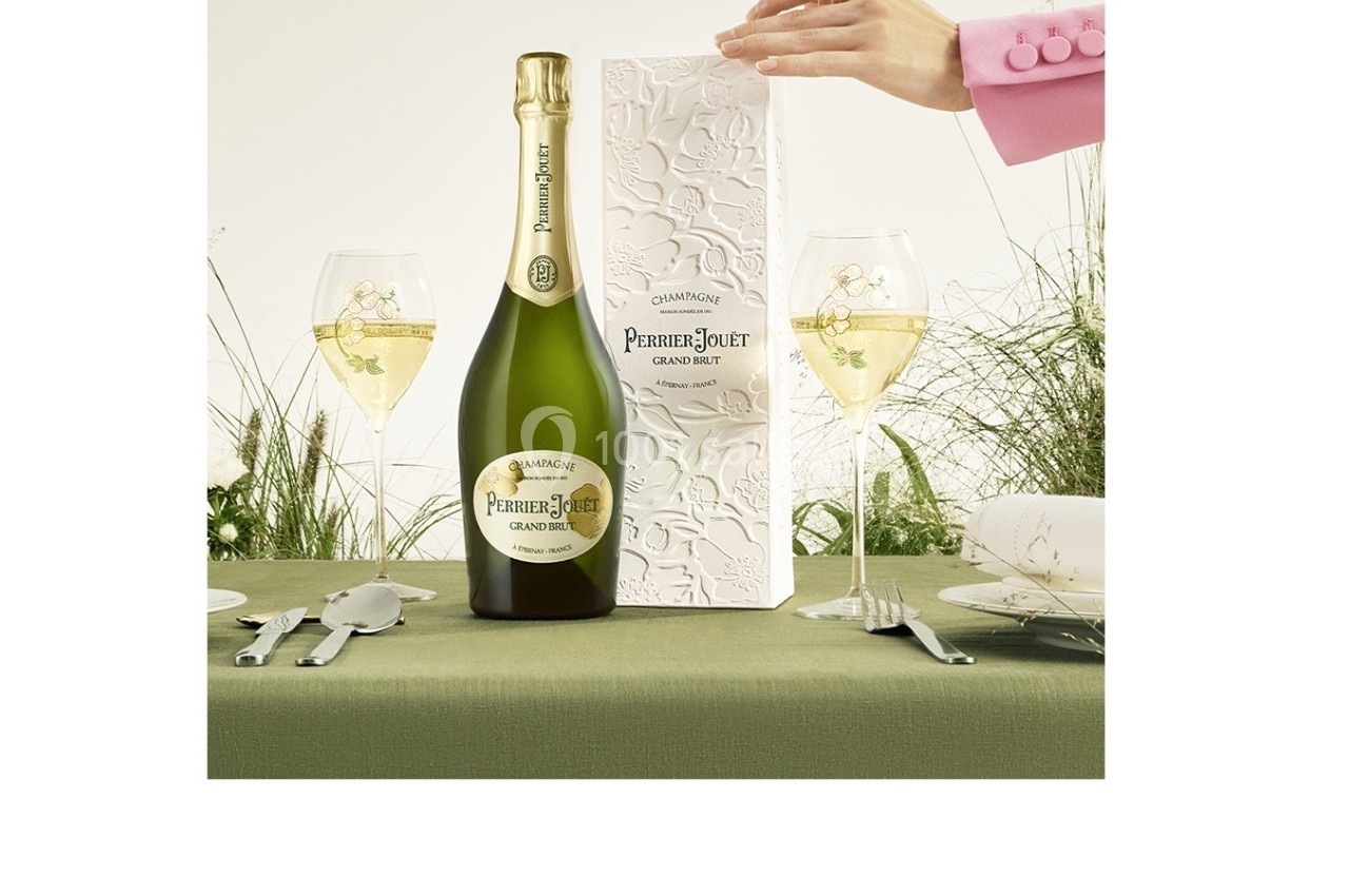 Bouteille de champagne avec son coffret décoré, posée sur une table dressée avec verres et couverts.