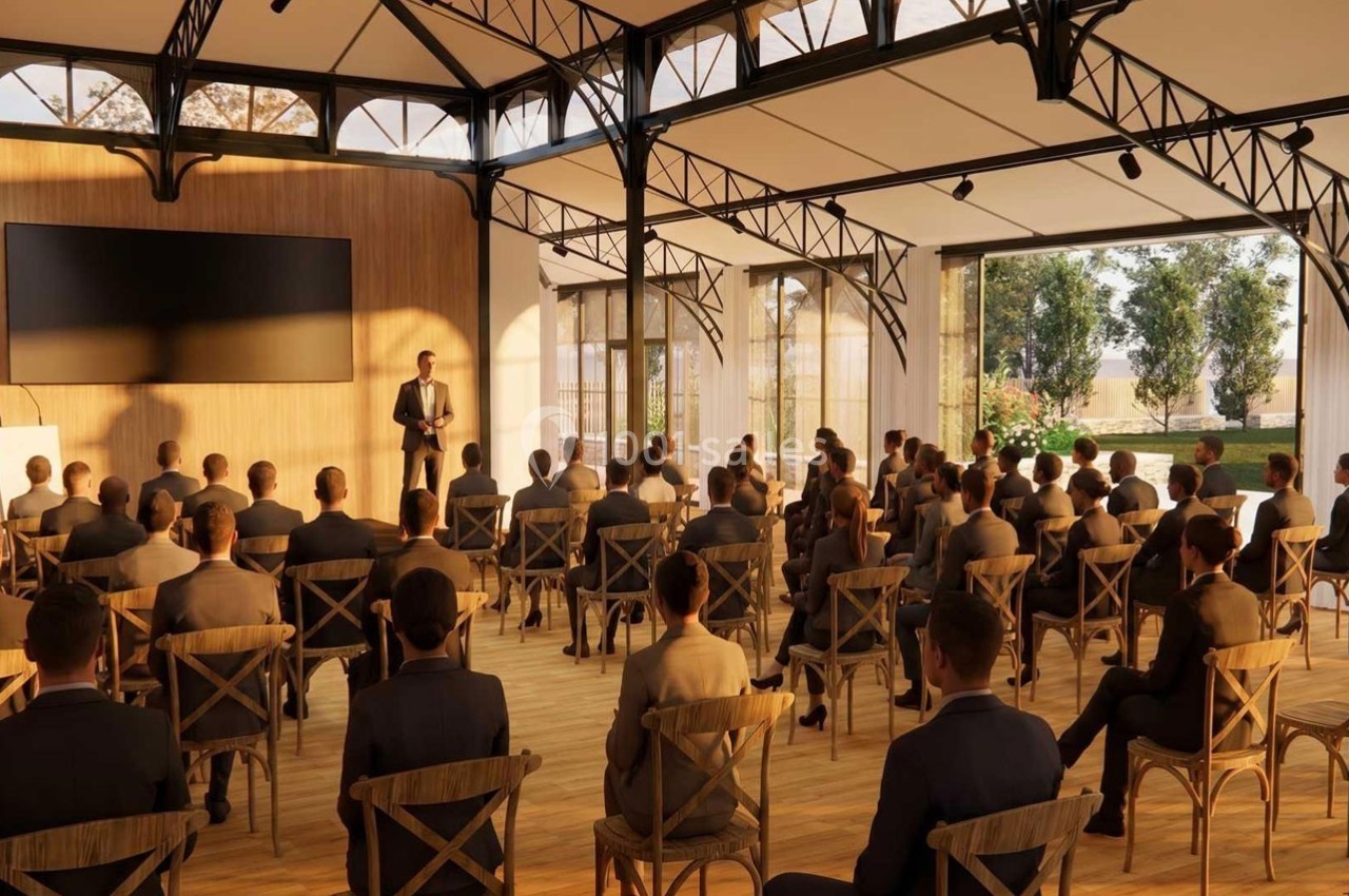 Un conférencier s'adresse à un public assis dans une salle lumineuse avec de grandes baies vitrées.
