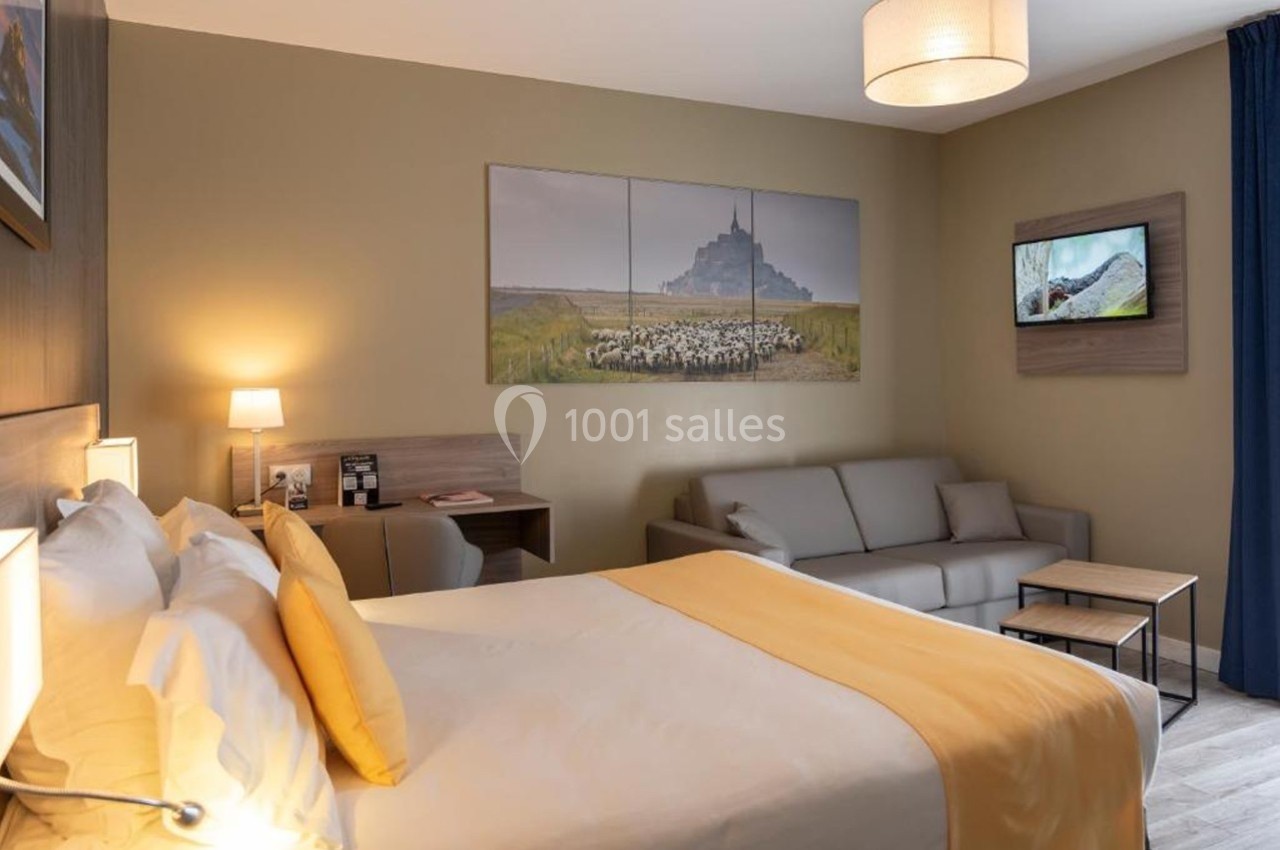 Chambre d'hôtel avec lit double, canapé, bureau, éclairage doux et décoration murale représentant des paysages.