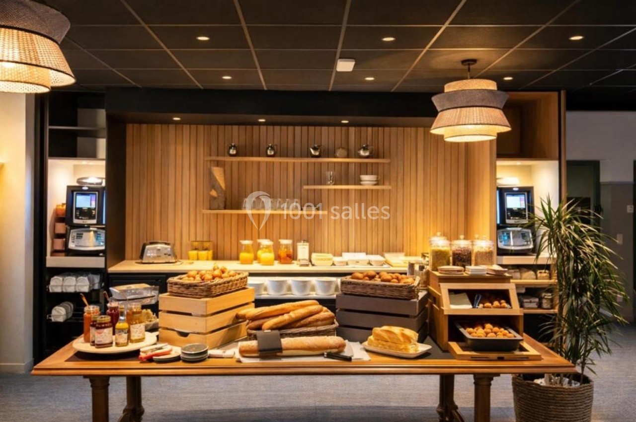 Buffet de petit-déjeuner avec pains, viennoiseries, confitures, céréales et boissons dans une salle lumineuse.