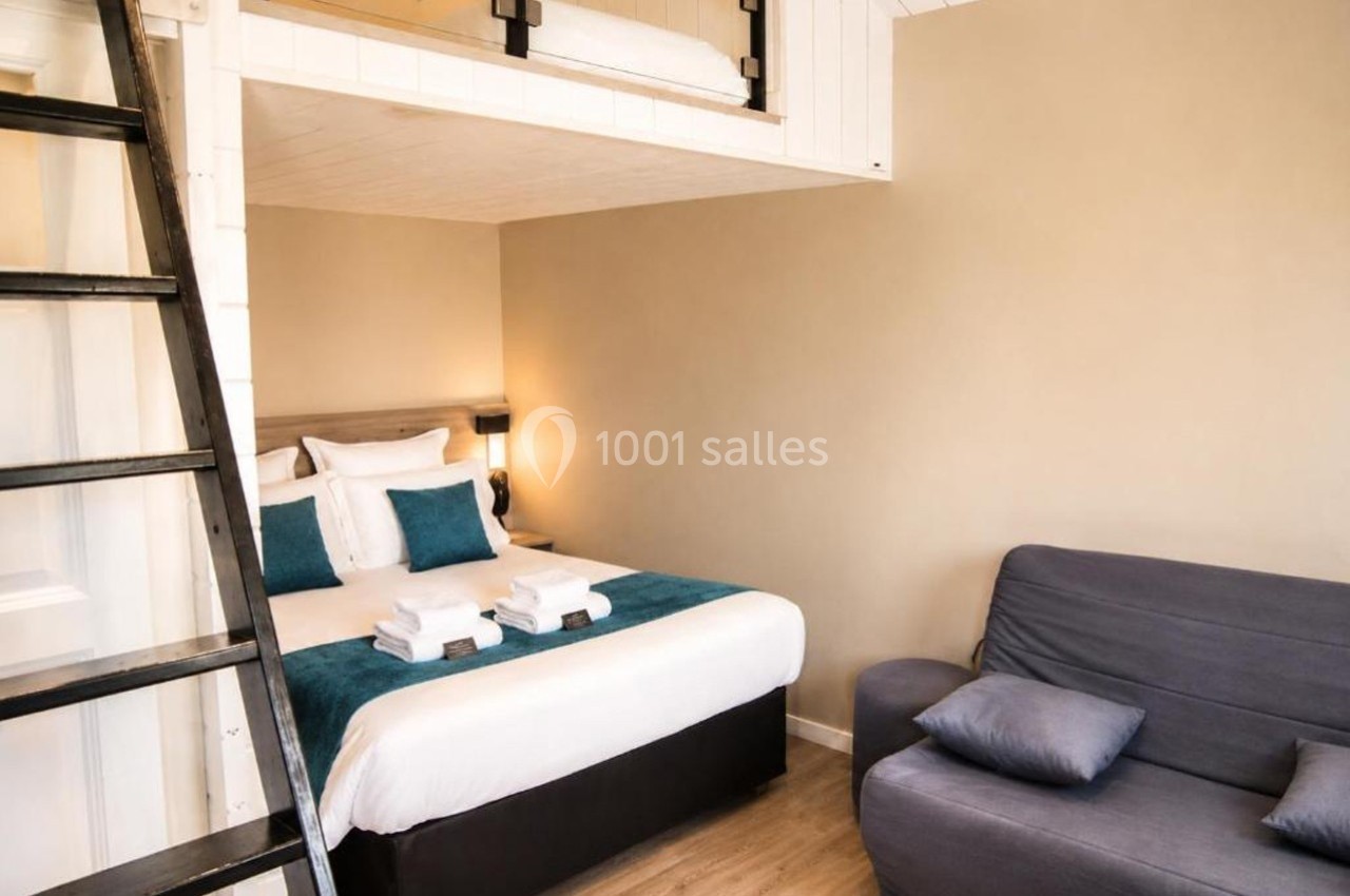 Chambre avec lit double, canapé, échelle menant à une mezzanine, décor moderne et tons neutres.