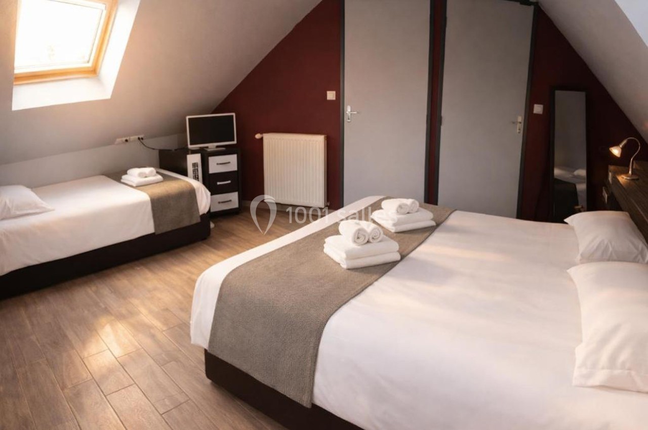 Chambre mansardée avec un lit double, un lit simple, un bureau, une télévision et une fenêtre de toit.