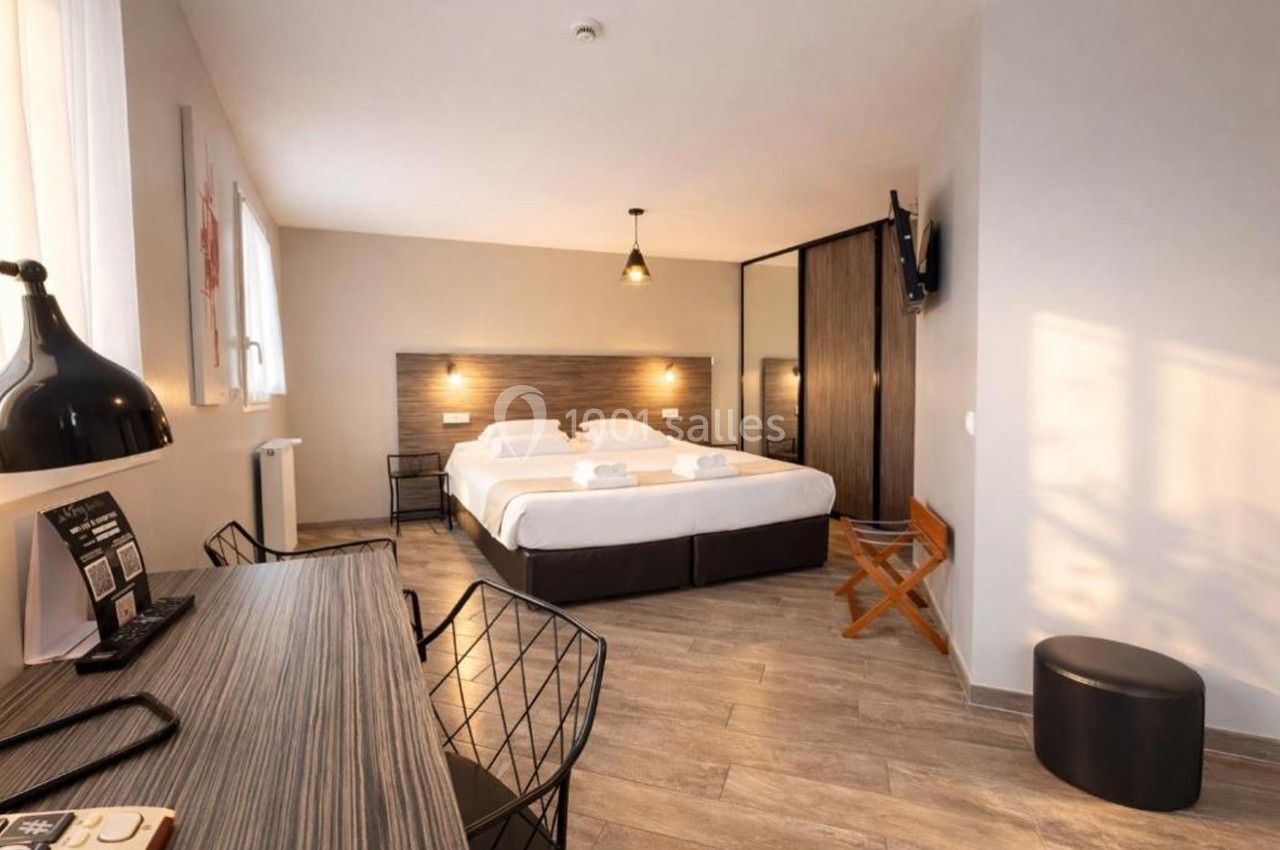 Chambre d'hôtel moderne avec deux lits simples, bureau, chaise, télévision murale et éclairage chaleureux.
