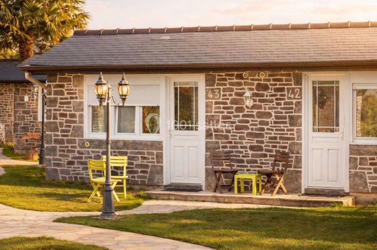 Façade d'un bâtiment en pierre avec portes blanches, mobilier de jardin coloré et allée en pierre sous une lumière douce.