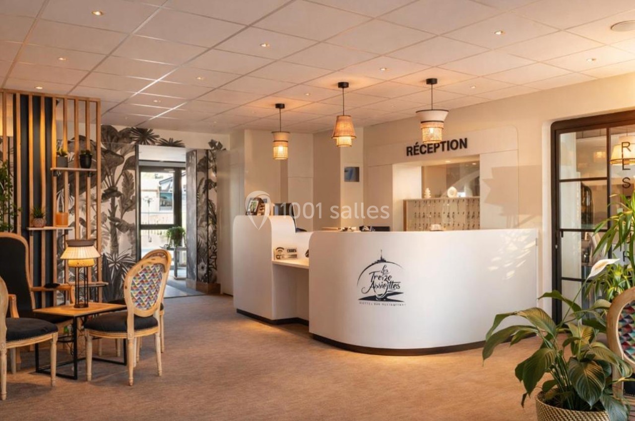Réception d'un hôtel avec comptoir blanc, chaises en bois, plantes et éclairage chaleureux.