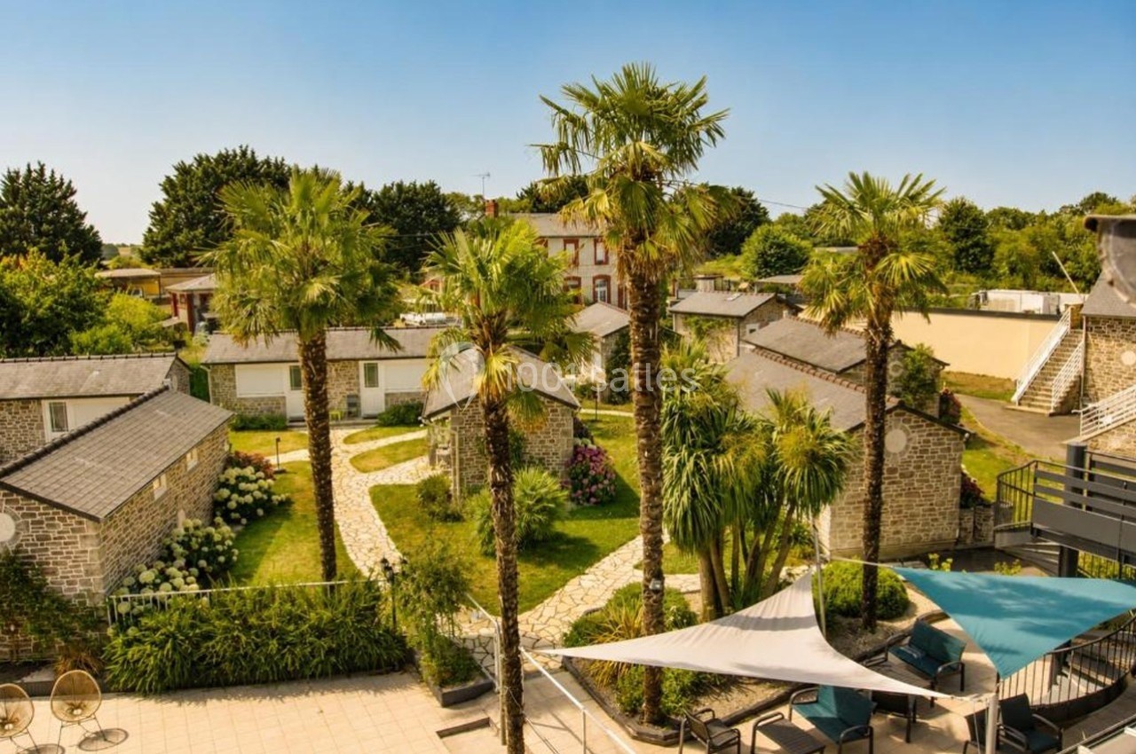 Vue d'un complexe de petites maisons en pierre entouré de palmiers et de jardins sous un ciel dégagé.