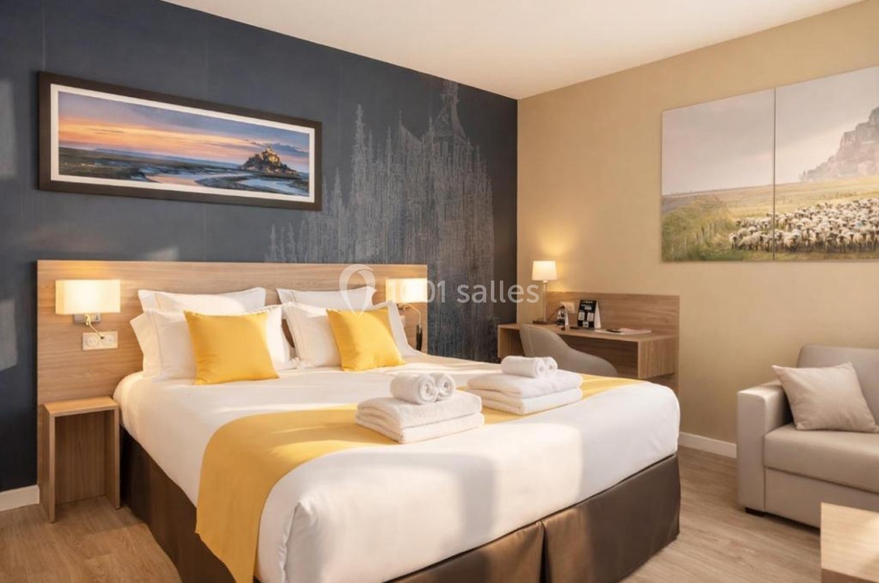 Chambre d'hôtel lumineuse avec un lit double, des coussins jaunes, un bureau, un canapé et des décorations murales.