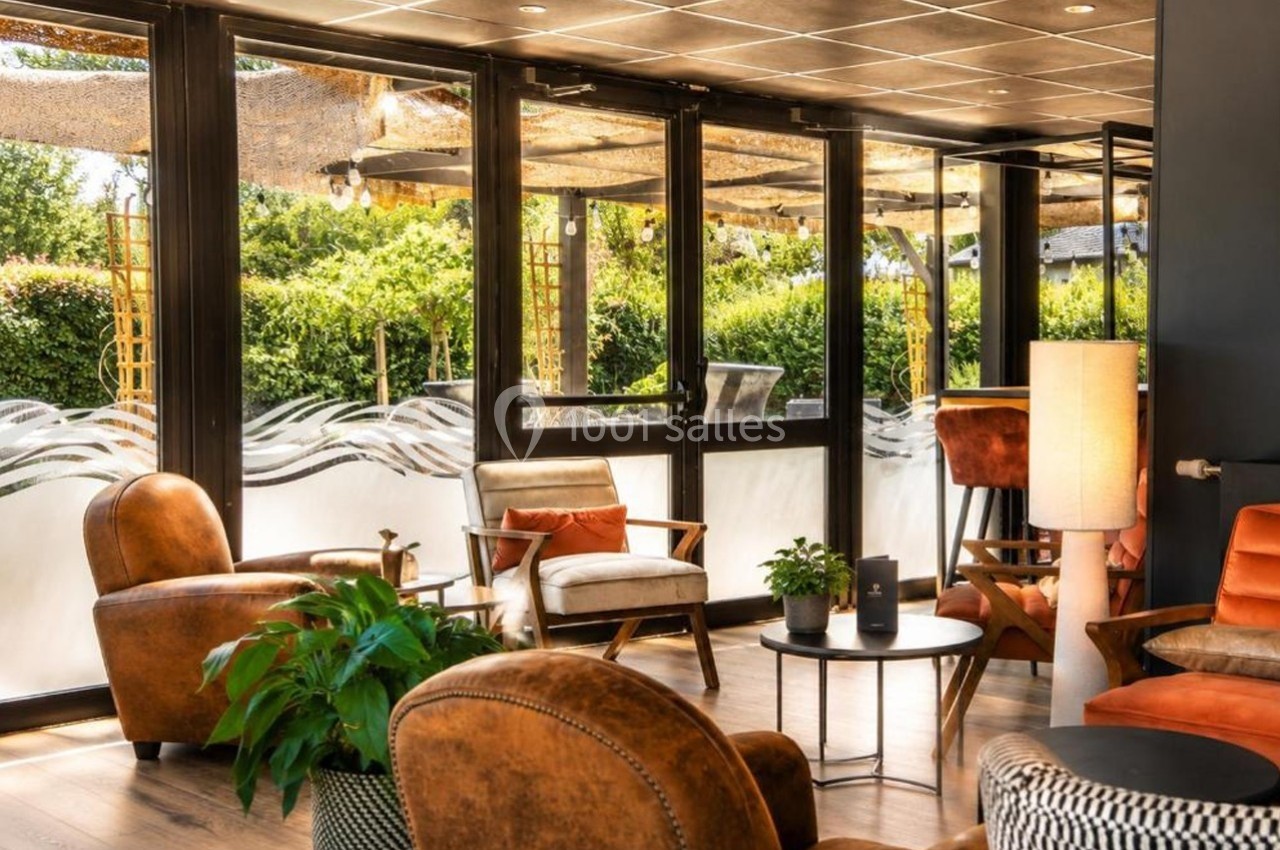 Espace intérieur lumineux avec fauteuils en cuir, plantes et grandes baies vitrées donnant sur un jardin verdoyant.