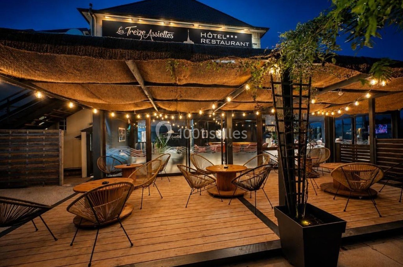 Terrasse d'un restaurant éclairée par des guirlandes lumineuses, avec des fauteuils en rotin et un toit en canisses.