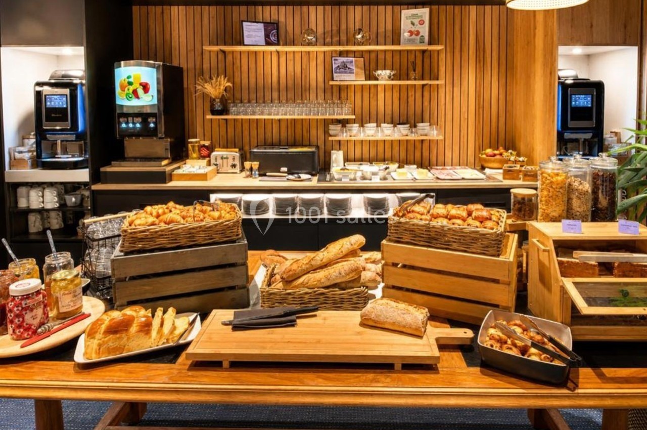 Buffet de petit-déjeuner avec pains, viennoiseries, céréales, confitures et boissons chaudes dans un cadre en bois.