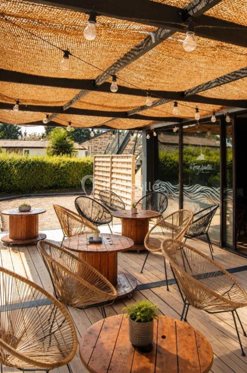 Terrasse en bois avec mobilier en rotin, tables rondes et toit en cannage laissant passer la lumière naturelle.
