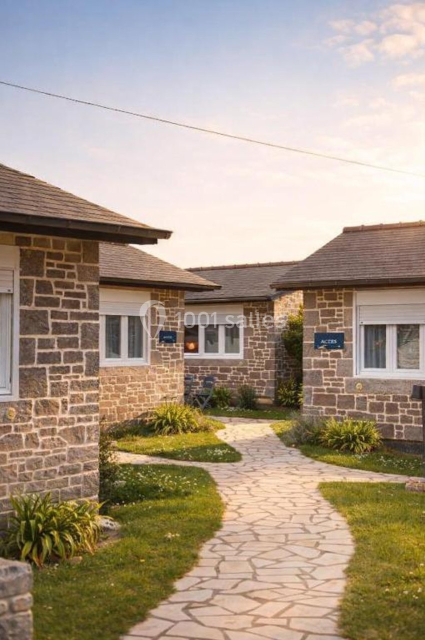 Allée pavée bordée de pelouses menant à des maisons en pierre sous un ciel légèrement nuageux.
