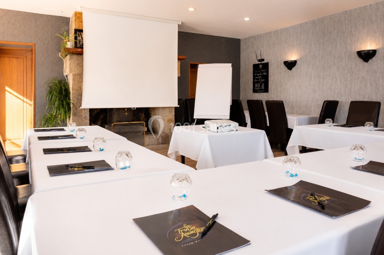 Salle de réunion lumineuse avec tables disposées en U, projecteur, écran, paperboard et documents sur les tables.