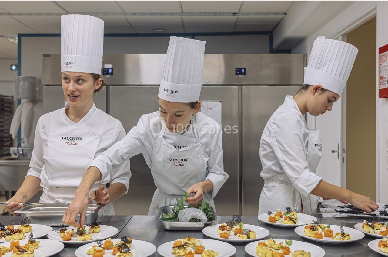 Trois cheffes en tenue blanche dressent des assiettes gastronomiques dans une cuisine professionnelle.